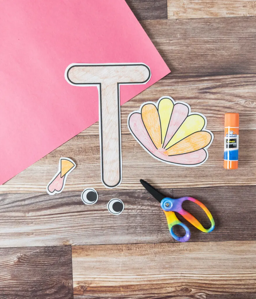 Red construction paper and all the parts for the letter T turkey craft colored and cut out. Scissors and glue stick laying beside them.