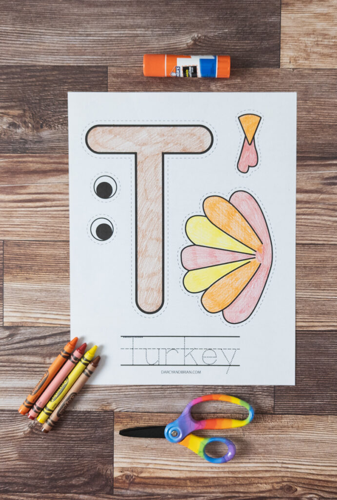 T for turkey printable craft colored in. Crayons, scissors and glue stick lay next to paper.