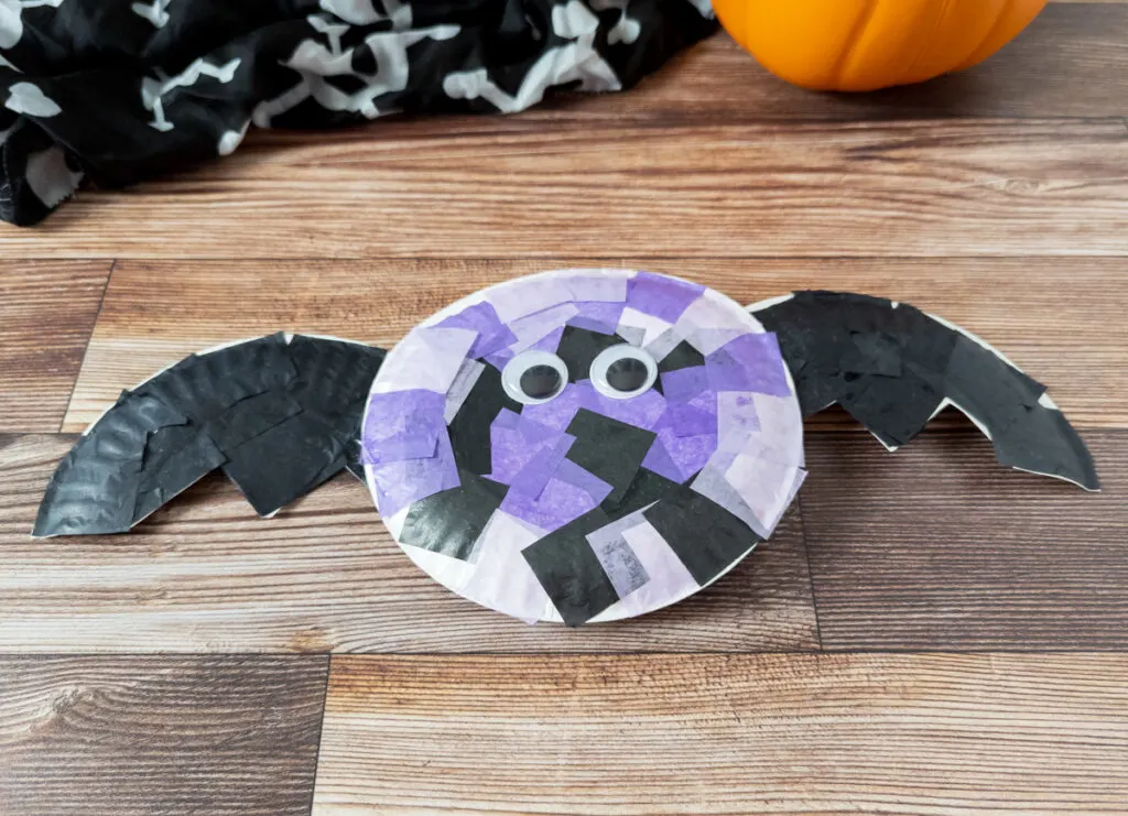 Completed tissue paper bat craft made with black and purple tissue paper squares and small round paper plates.