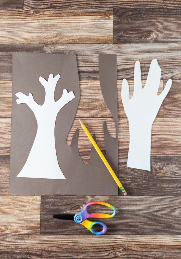 Tree template and traced hand cut out of white cardstock. Tree template laying on brown paper to be traced.