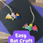 Two wooden bat shapes covered in colorful tissue paper with twine to hang them. They are laying on top of black and purple construction paper.