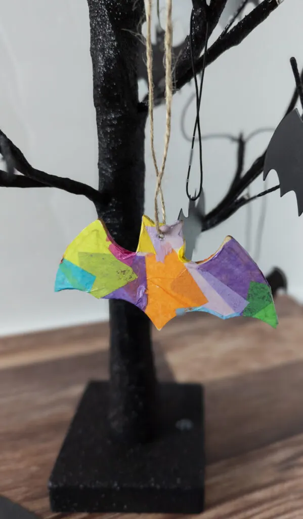 Close view of colorful bat ornament hanging from small black Halloween tree.