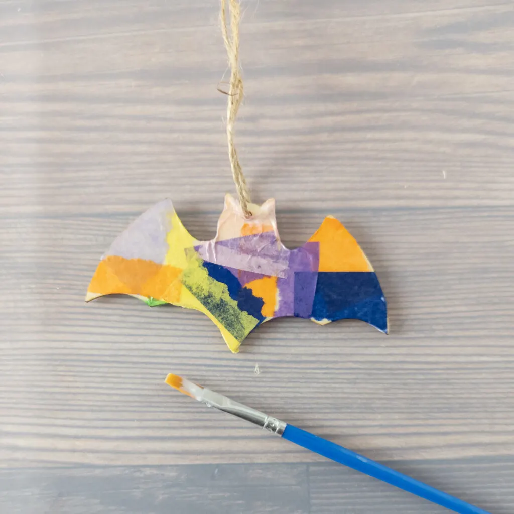 Close view of wooden bat covered with tissue paper pieces and a layer of glue applied to seal it. Tissue paper neatly pressed around edges.