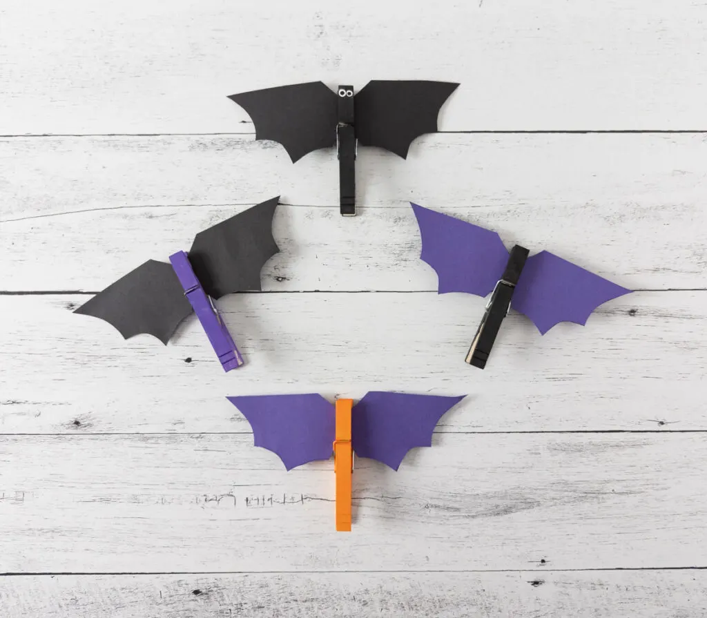 Four completed clothespin bats. One is black with black wings, one is black with purple wings, one is purple with black wings, and one is orange with purple wings.