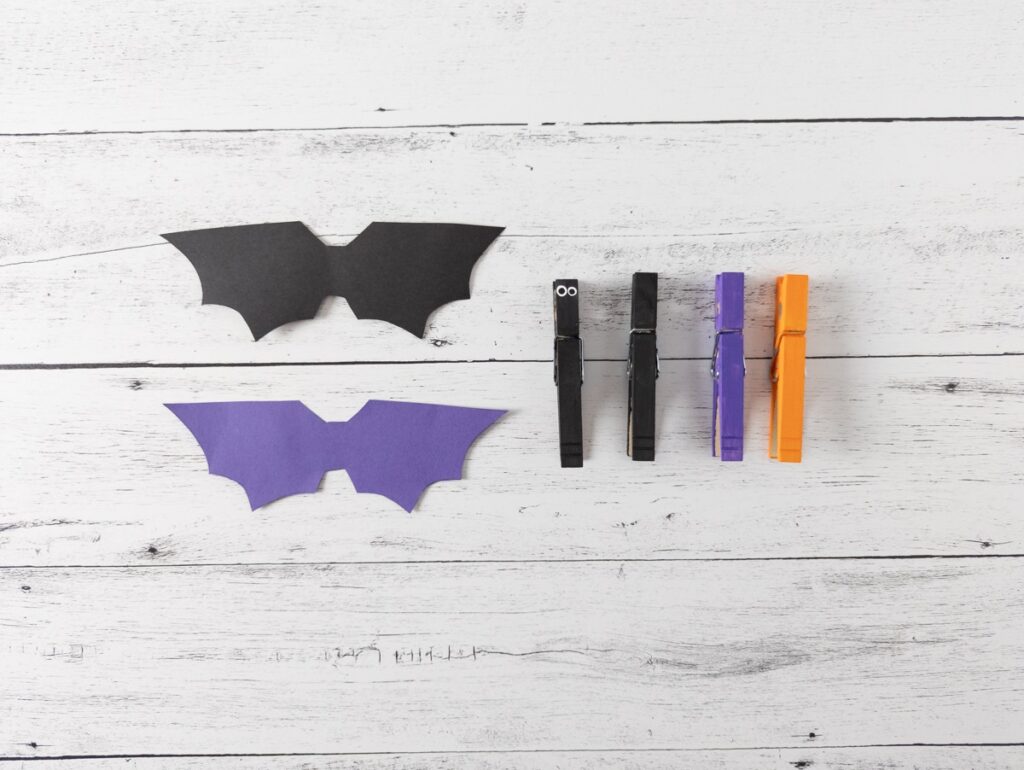 Black and purple bat wings cut out and laying next to row of painted clothespins.