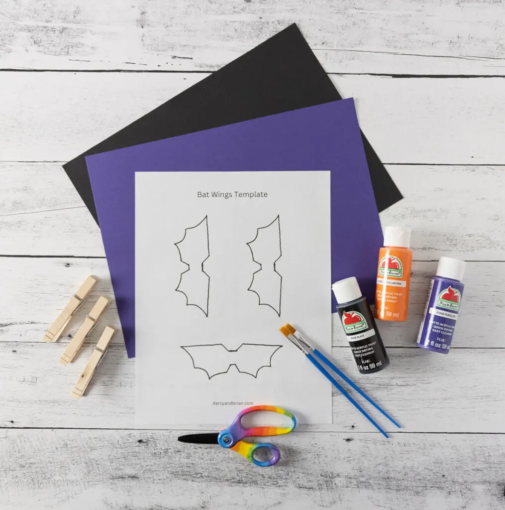 Black and purple construction paper, bat wing template, wooden clothespins, scissors, paint brushes, black, orange, and purple paint.