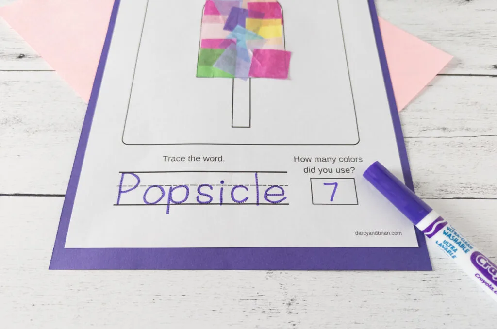 Angled view of the word popsicle traced with a purple marker and the number 7 under a multi-colored popsicle craft.