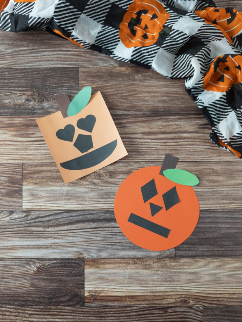 Completed shape pumpkin crafts on table (one circle and one square) next to black and white plaid fabric with jack-o-lanterns on it.