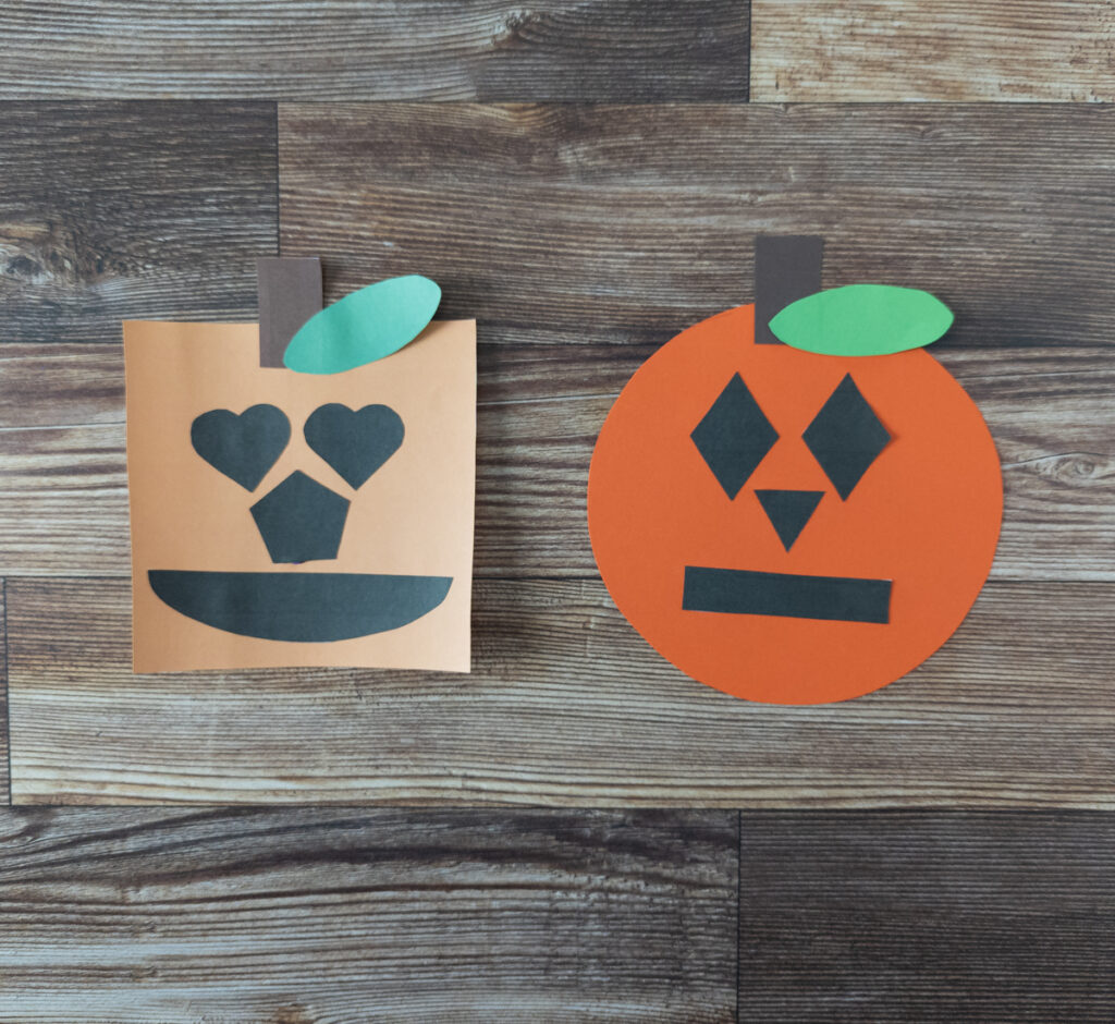 Two finished shape pumpkin crafts laying next to each other on table. Left one is square with hearts, pentagon, and semi-circle face pieces. Left one made from printing out color version. Right pumpkin is a circle shape cut out from construction paper with diamonds, triangle, and rectangle features.