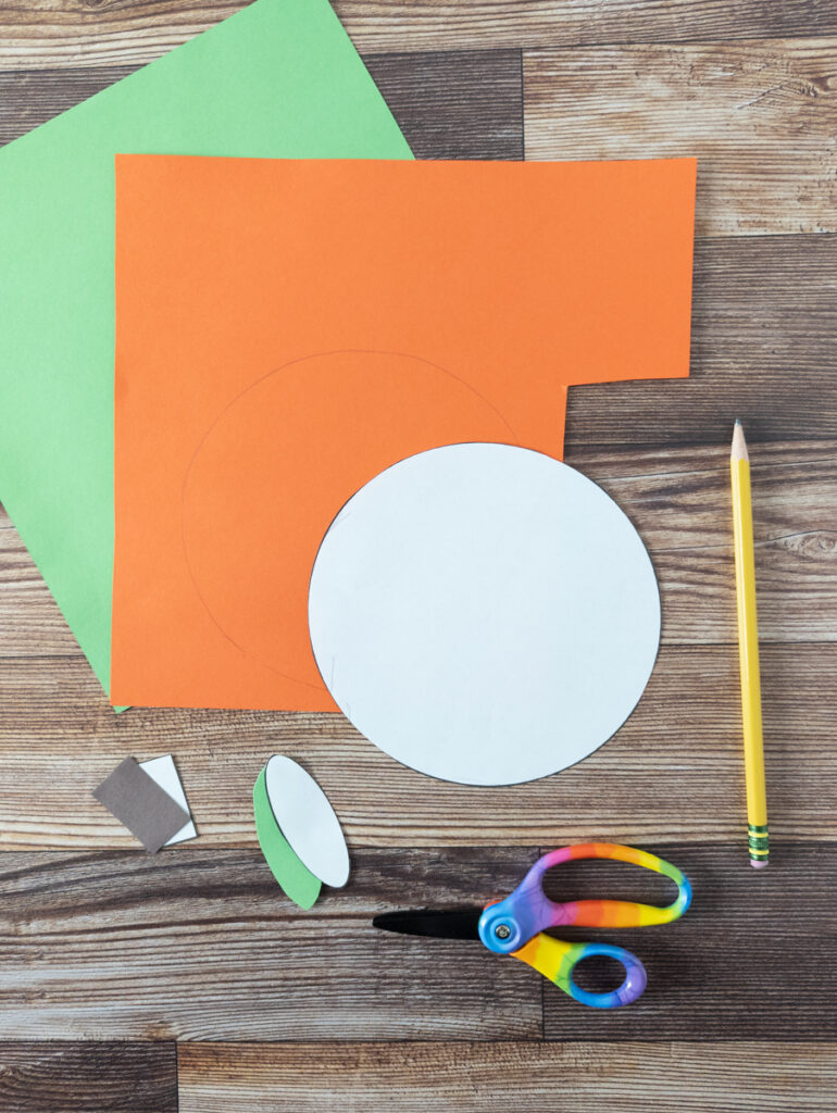 Using shape pumpkin craft templates to trace and cut out of brown, green, and orange construction paper.