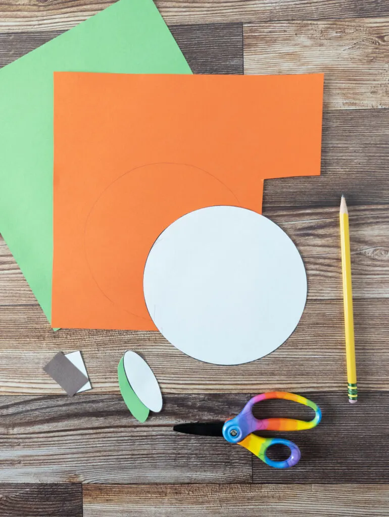 Using shape pumpkin craft templates to trace and cut out of brown, green, and orange construction paper.