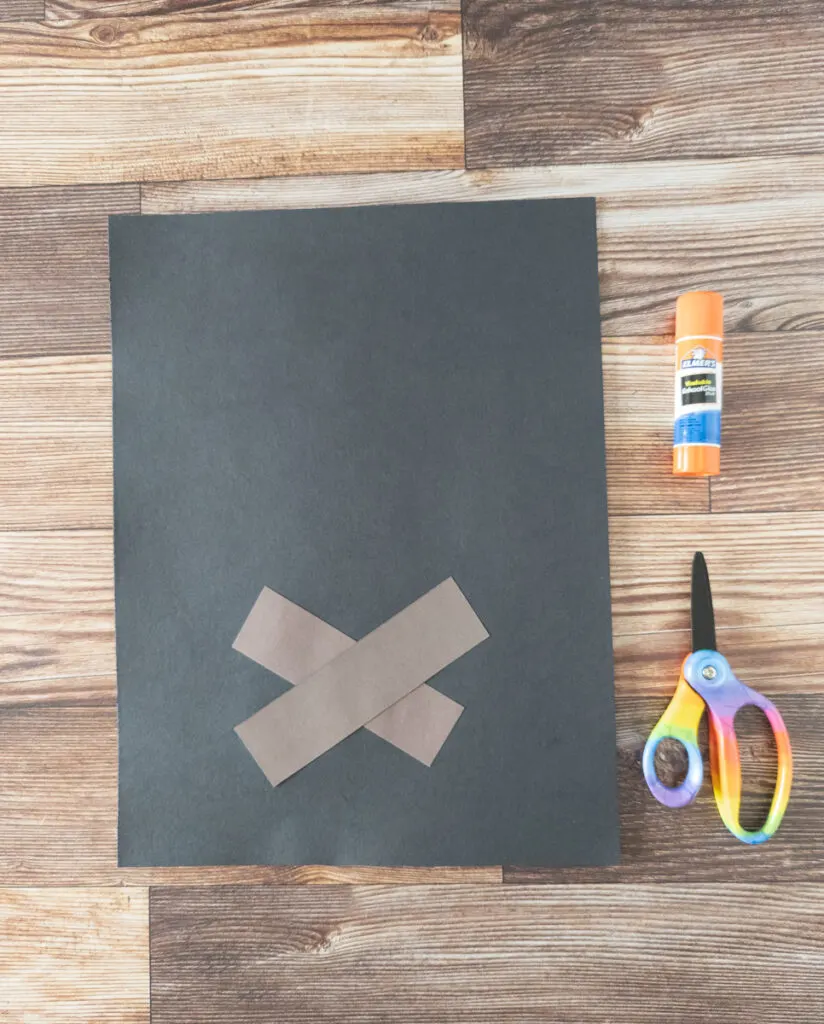 Two rectangles of brown construction paper glued in the shape of the letter X on a black piece of paper.