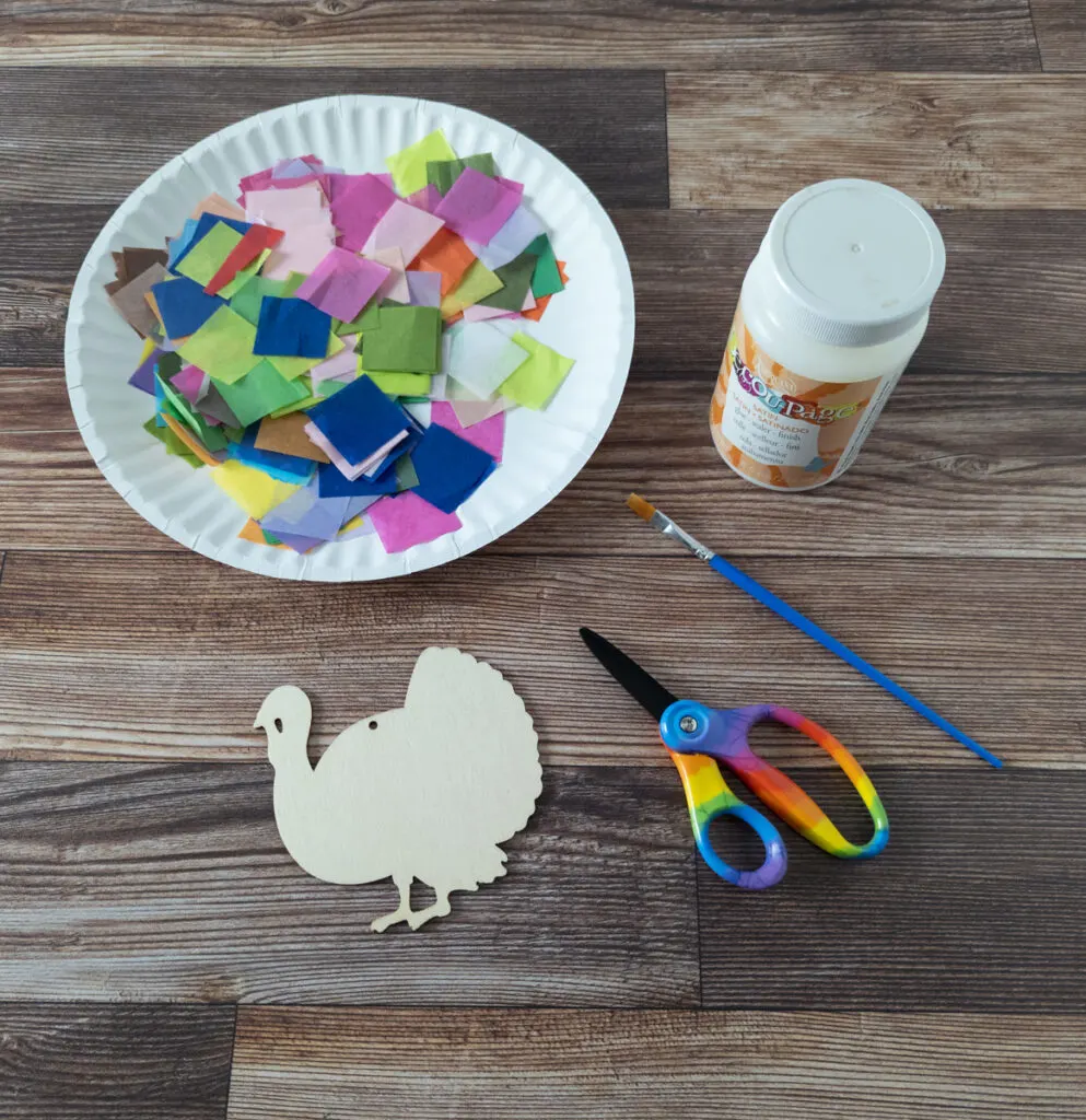 Assorted tissue paper squares, decoupage glue, small paint brush, scissors, and wooden turkey cutout for Thanksgiving craft project.