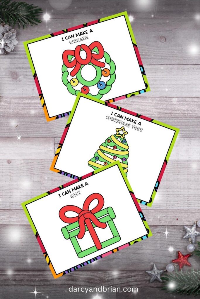 Mockup with three full color holiday playdough mats featuring a present, a Christmas tree, and a wreath overlapping each other on a gray wood background with little stars.