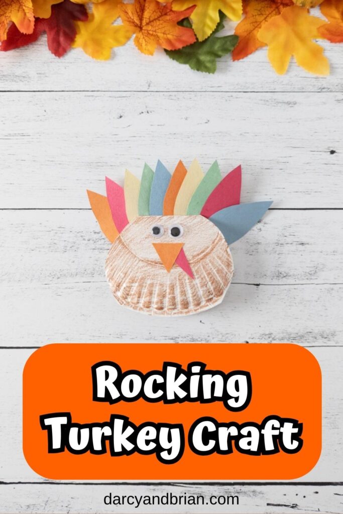 Completed turkey craft made with a folded paper plate and construction paper. White and black text on orange near the bottom says Rocking Turkey Craft.