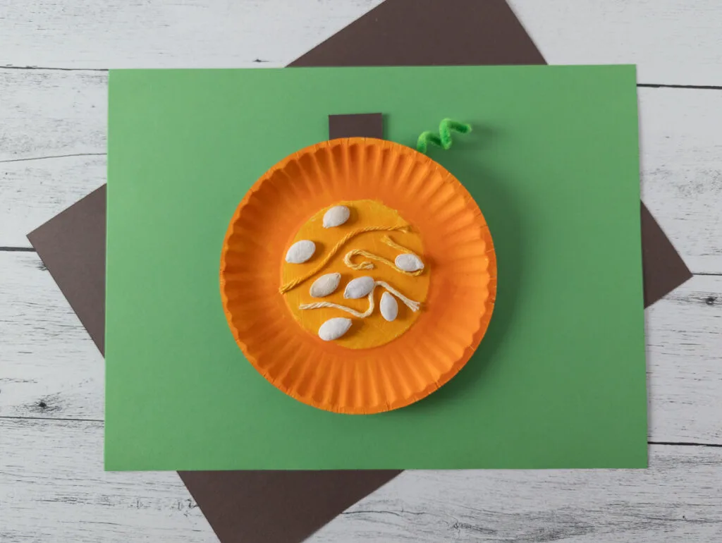 Completed parts of a pumpkin craft showing what the inside of a pumpkin looks like. Pumpkin craft laying on top of green and brown paper.