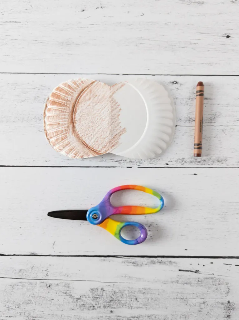 Small paper plate cut and folded open to color with a brown crayon. It is halfway colored.