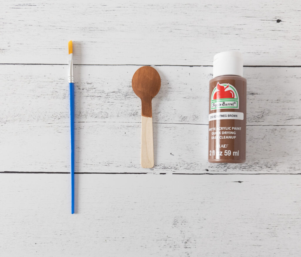 Paint brush, partially painted spoon, and brown paint bottle.