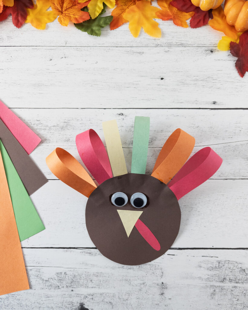 Cute paper turkey craft project next to assorted construction paper.