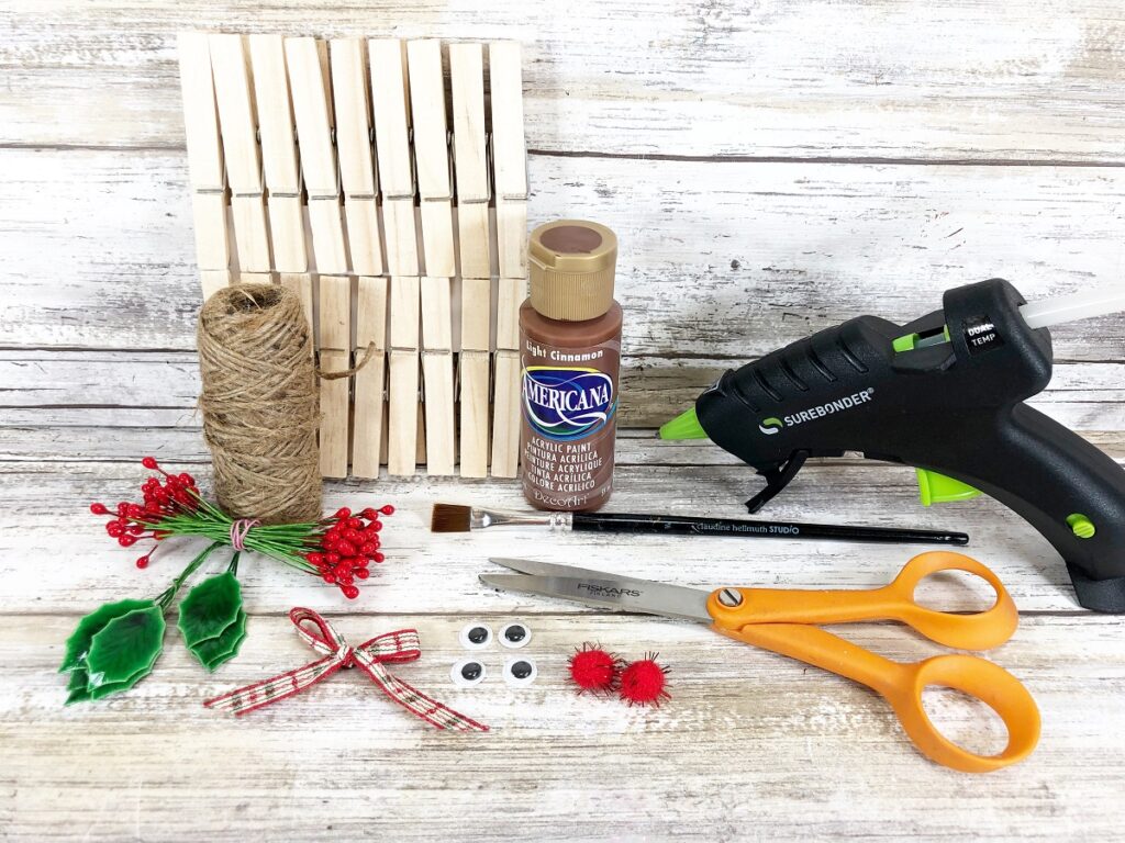 Wood clothespins, twine, brown paint, ribbon, little red pom poms, scissors, glue gun, bow, and faux holly and berries.