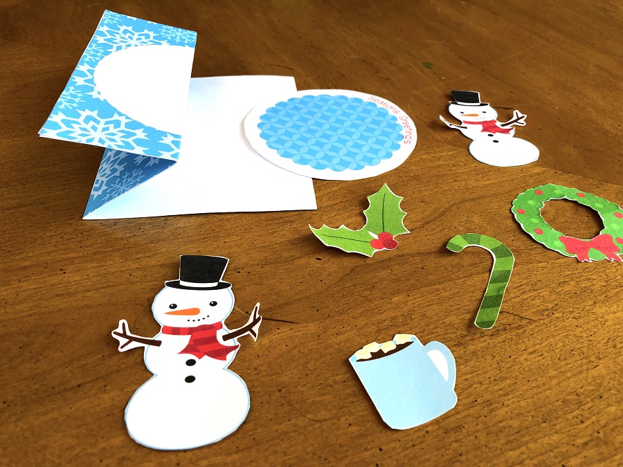 All the card embellishments cut out: snowmen, hot chocolate, holly, candy cane, and wreath. Card base shows how the z fold should look.
