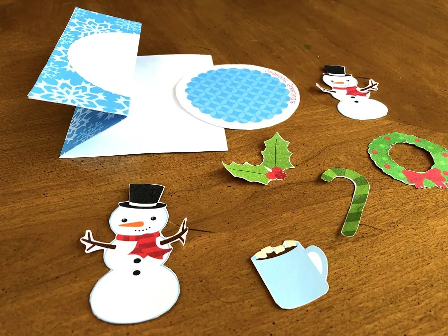 All the card embellishments cut out: snowmen, hot chocolate, holly, candy cane, and wreath. Card base shows how the z fold should look.