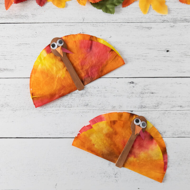 Two finished coffee filter turkey crafts made with mini spoons and dyed coffee filters. Fall leaves and pumpkins along the top.