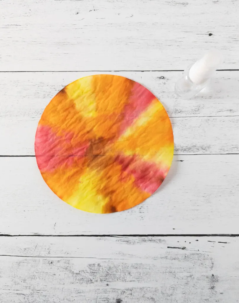 Coffee filter with red, yellow, orange, and brown marker ink blended and dried. Finger tip spray bottle next to it.