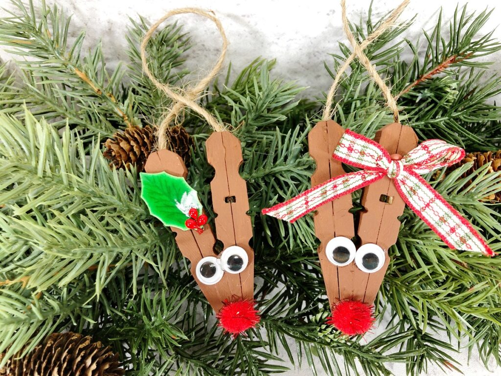 Two finished clothespin reindeers, one with a holly leaf and one with a bow on the antler.