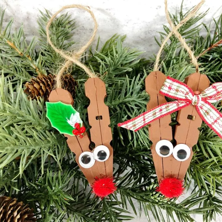 Two finished clothespin reindeers, one with a holly leaf and one with a bow on the antler.