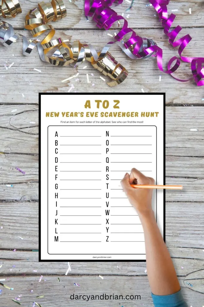Mockup of New Year's Eve A to Z scavenger hunt worksheet and older kid's hand holding a pencil over the paper.
