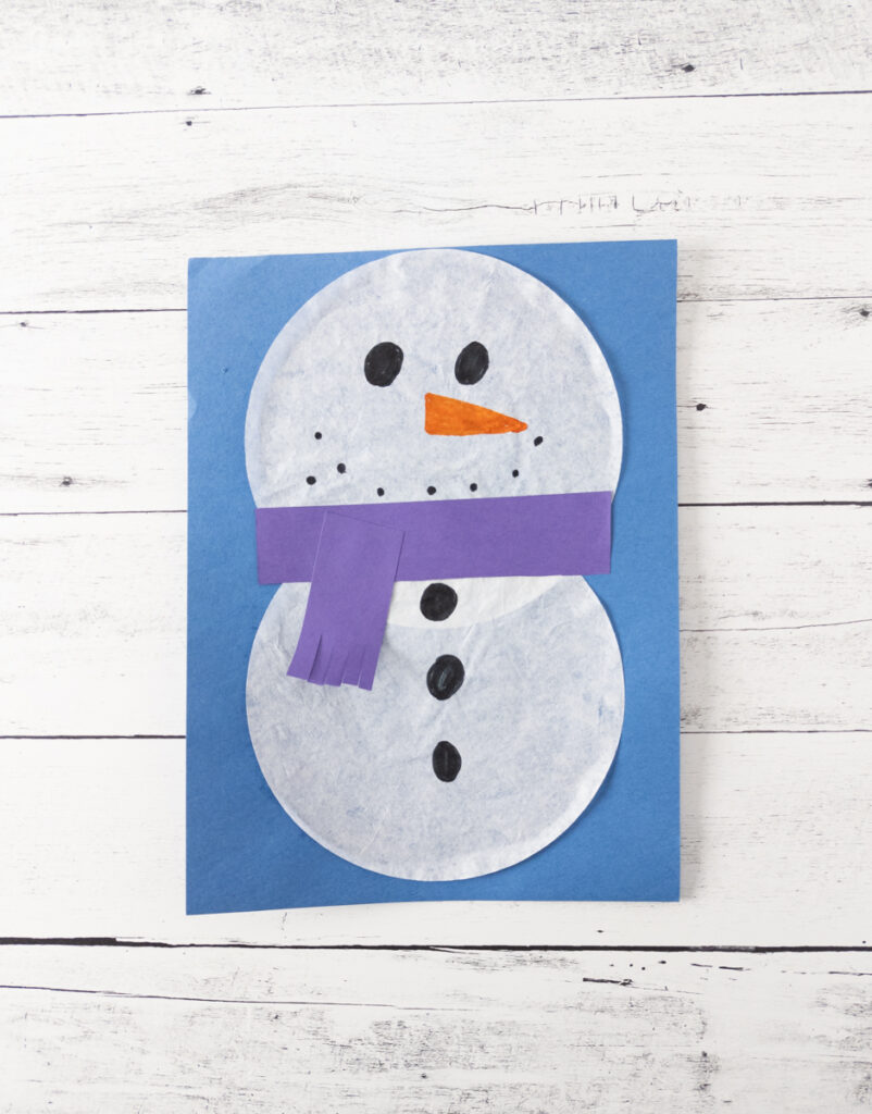 Snowman made with two coffee filters and a purple construction paper scarf glued onto blue paper.