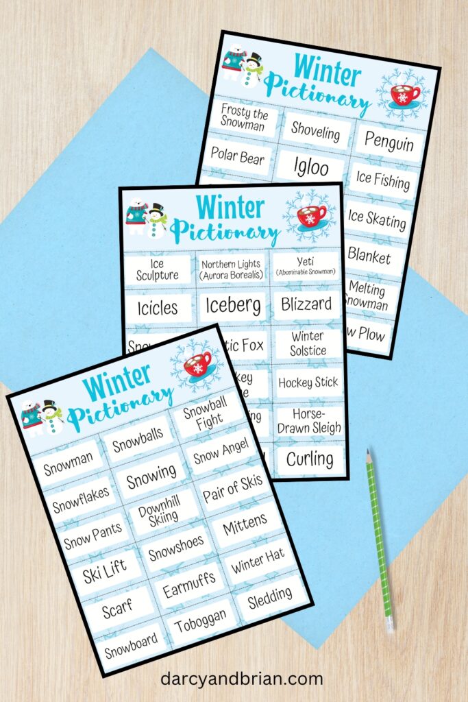 Mockup of three pages of Winter Pictionary word cards with a blue paper and desk background.