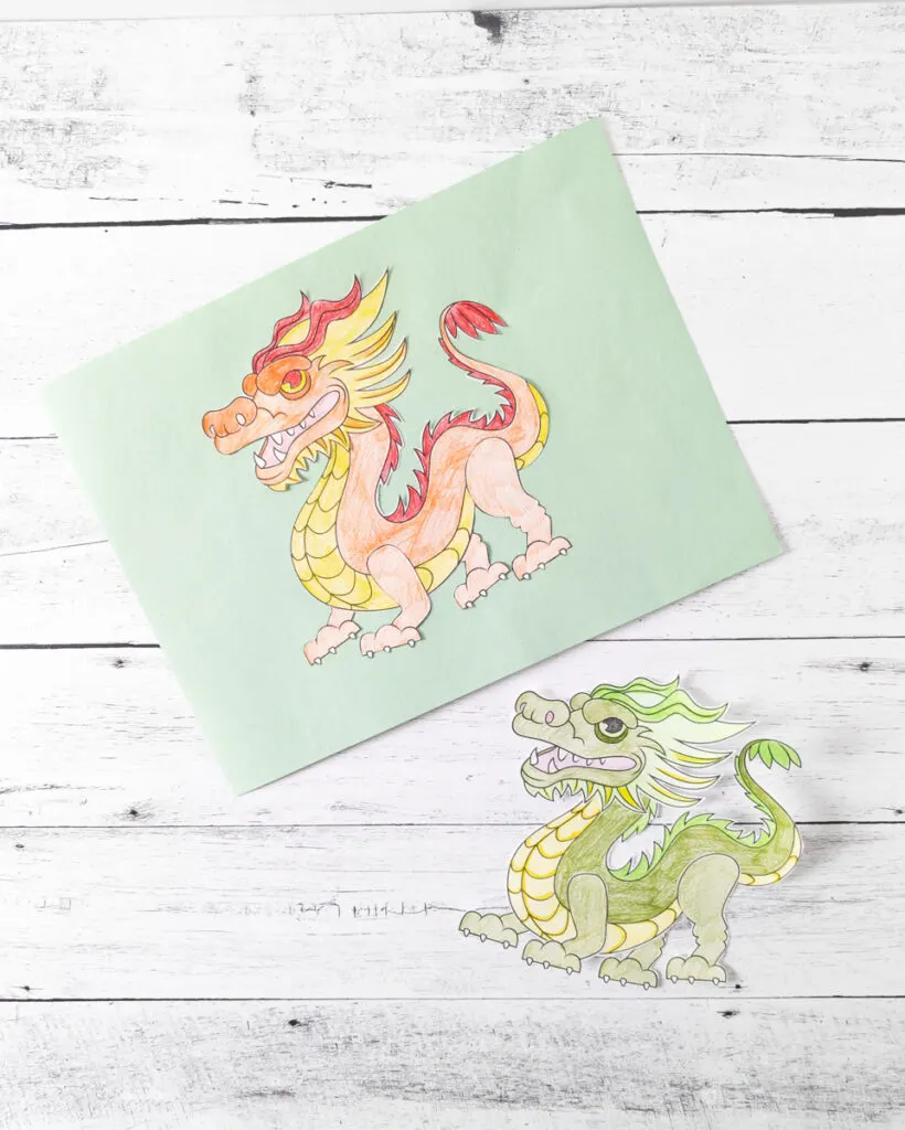 Red and and orange build a dragon glued to light green paper. Green dragon cut out and laying on table.