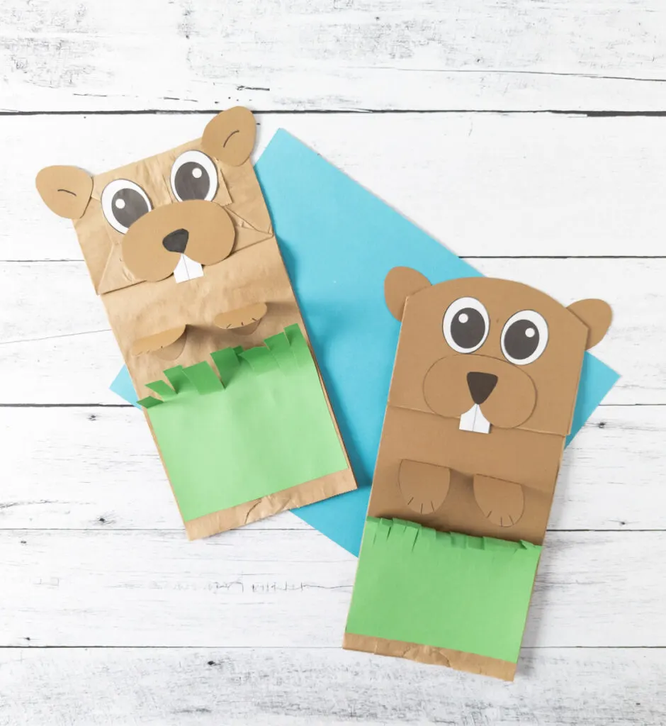 Two paper bag groundhog puppets laying on a bright blue paper.