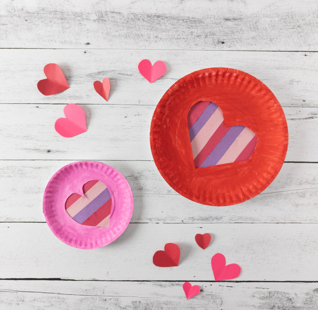 Two completed valentine crafts made with paper plates. One red and one pink.