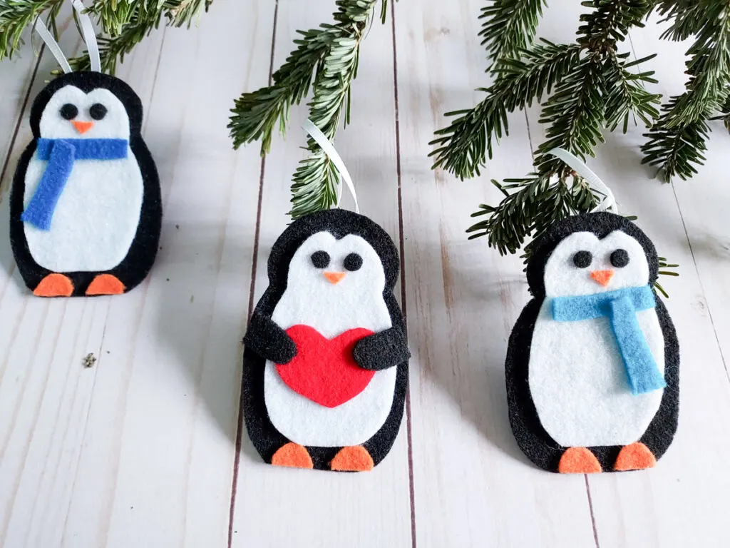 Three completed penguin ornaments made out of felt hanging from a Christmas tree.