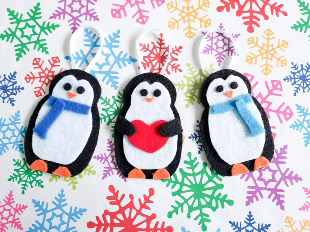 Three penguin crafts for kids laying on top of colorful snowflake paper.