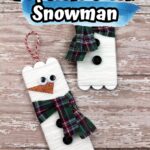 Completed popsicle stick snowman crafts laying on a wood background.
