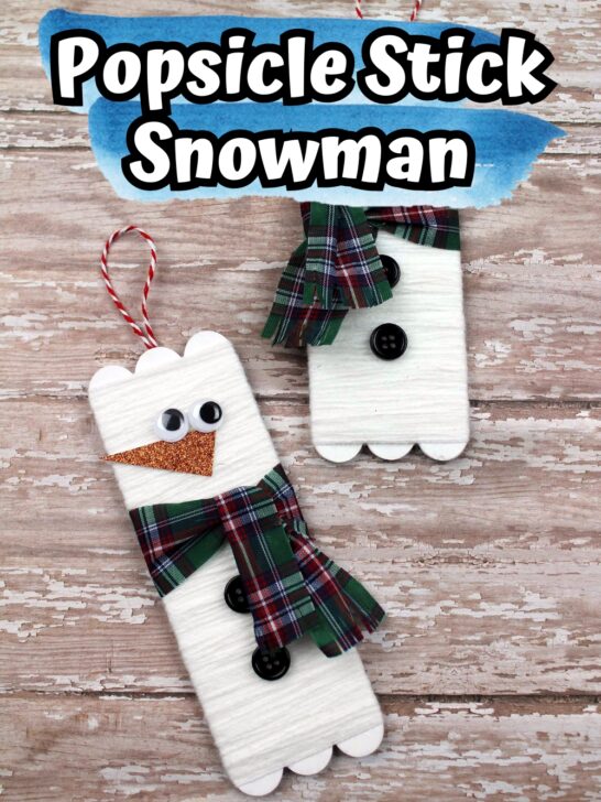 Completed popsicle stick snowman crafts laying on a wood background.