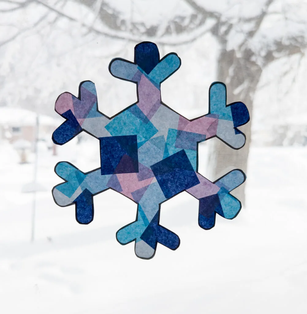 Snowflake tissue paper suncatcher in the window with lots of snow outside.