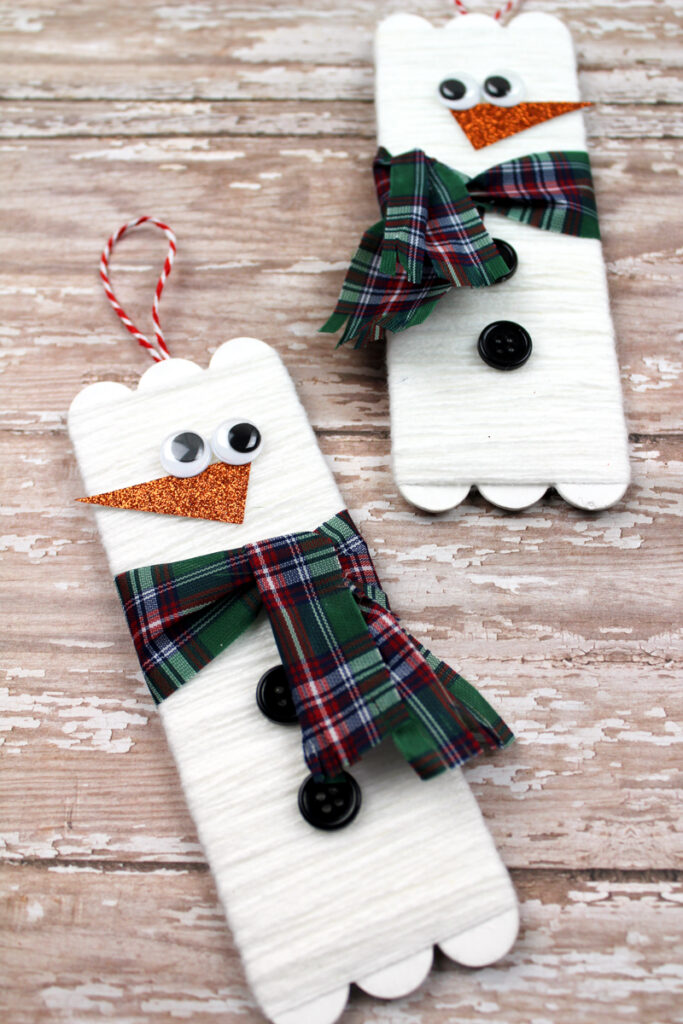 Two yarn wrapped snowman popsicle stick craft projects.