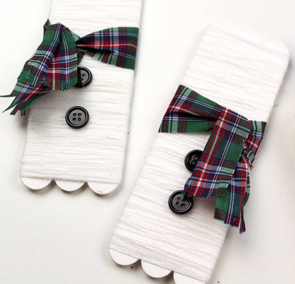 Yarn wrapped craft sticks with plaid ribbon tied around the middle and black buttons glued on.