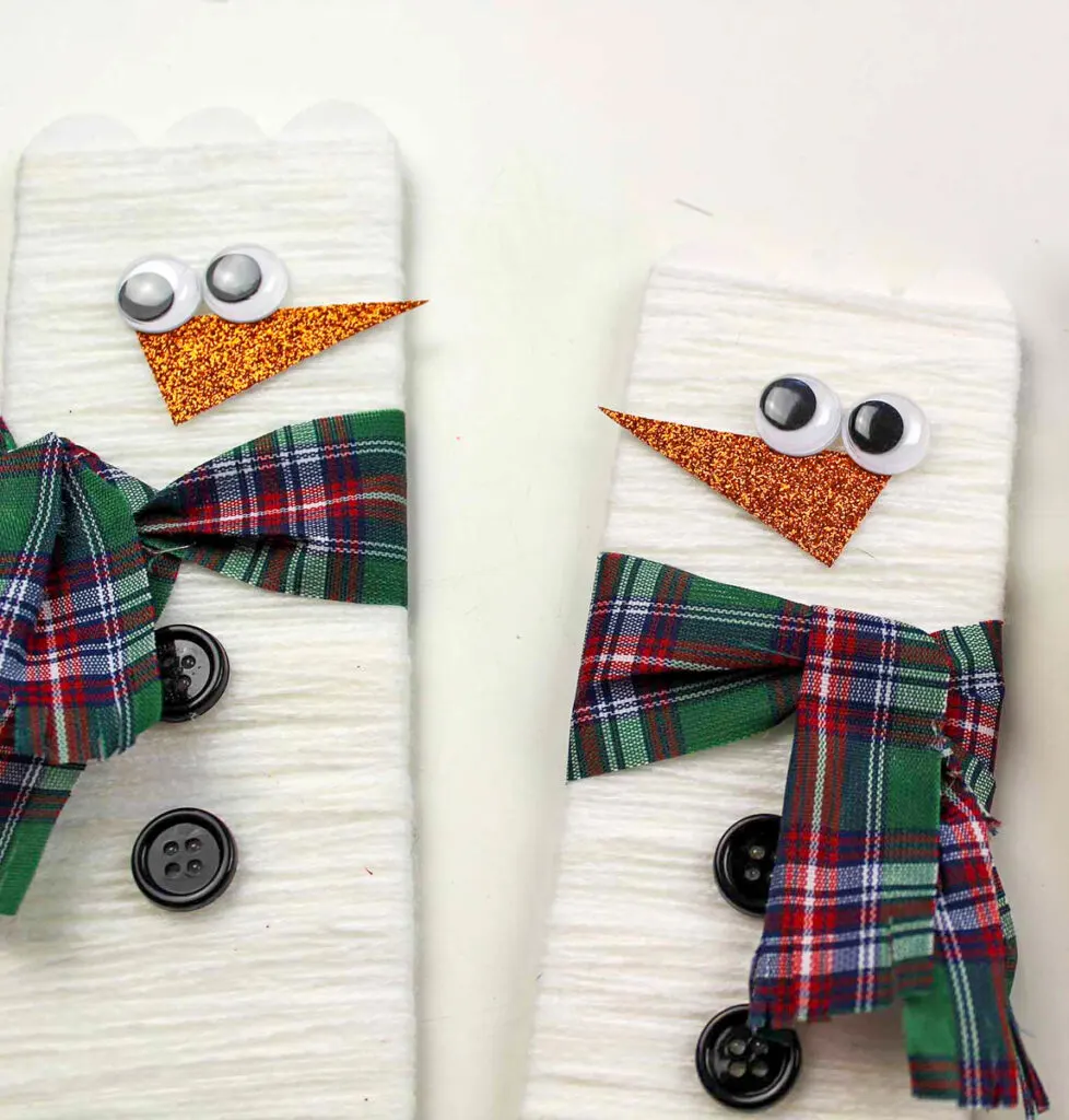 Adding eyes and nose to snowman popsicle stick crafts.