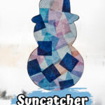 Completed snowman suncatcher craft made with tissue paper in a sunny window during winter.