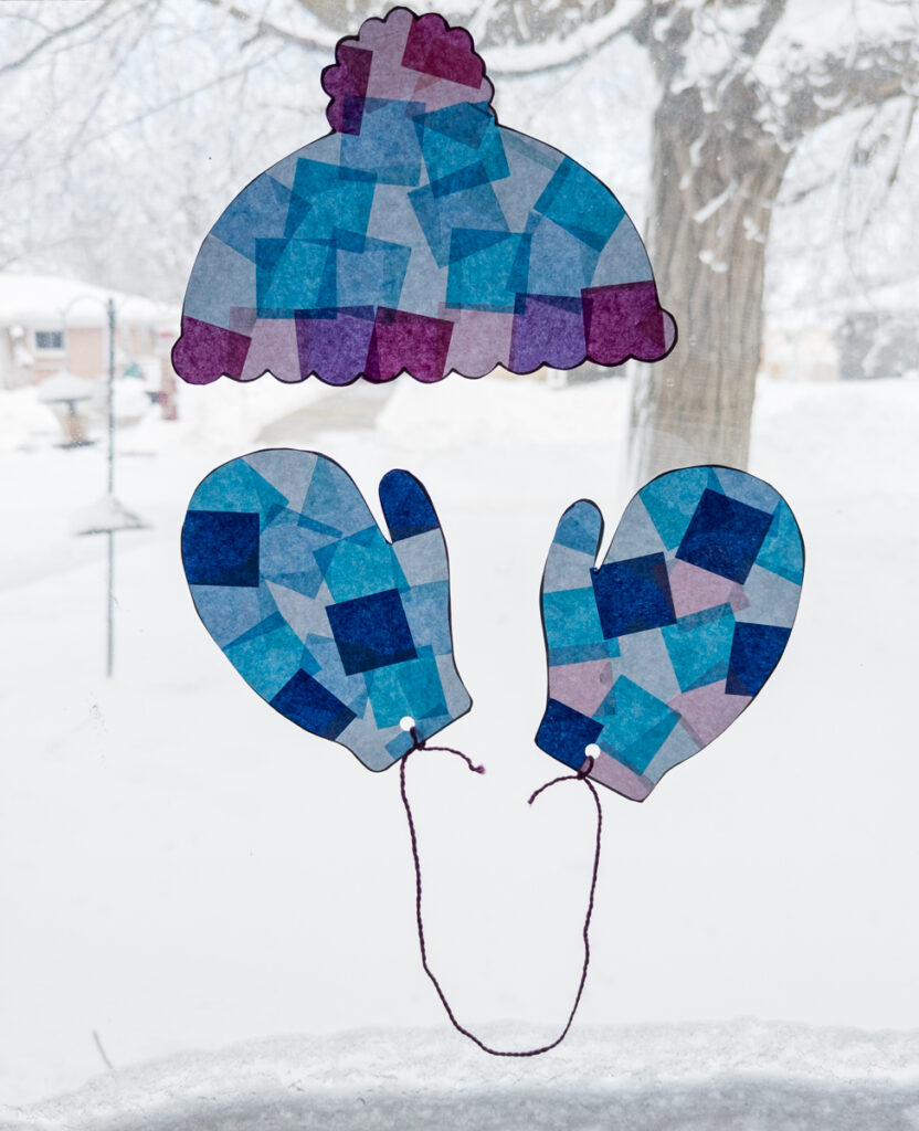 Finished winter themed suncatcher crafts made with tissue paper hanging in the window.