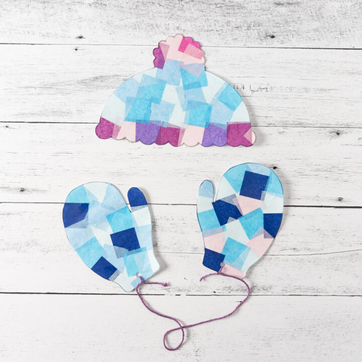 Winter hat and mittens suncatchers cut out. Mittens hole punched and tied together with purple yarn.