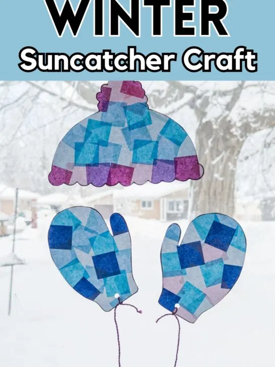 Completed hat and mittens winter suncatcher craft made with tissue paper hanging in a bright, snowy window.
