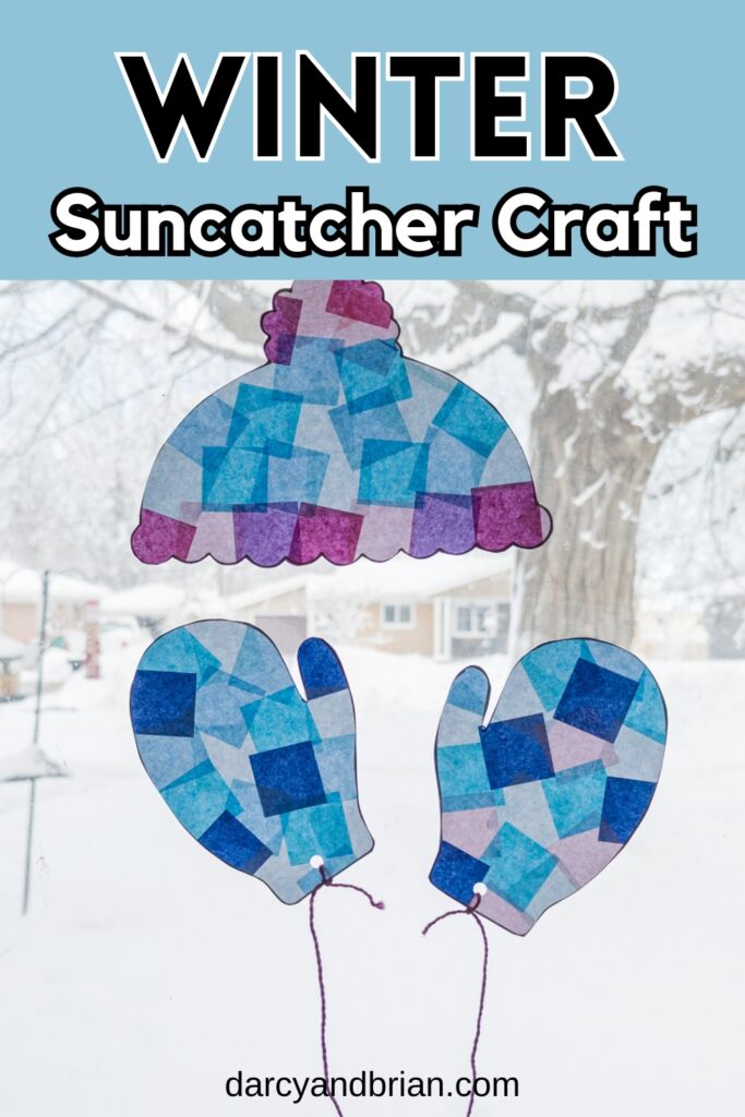 Completed hat and mittens winter suncatcher craft made with tissue paper hanging in a bright, snowy window.