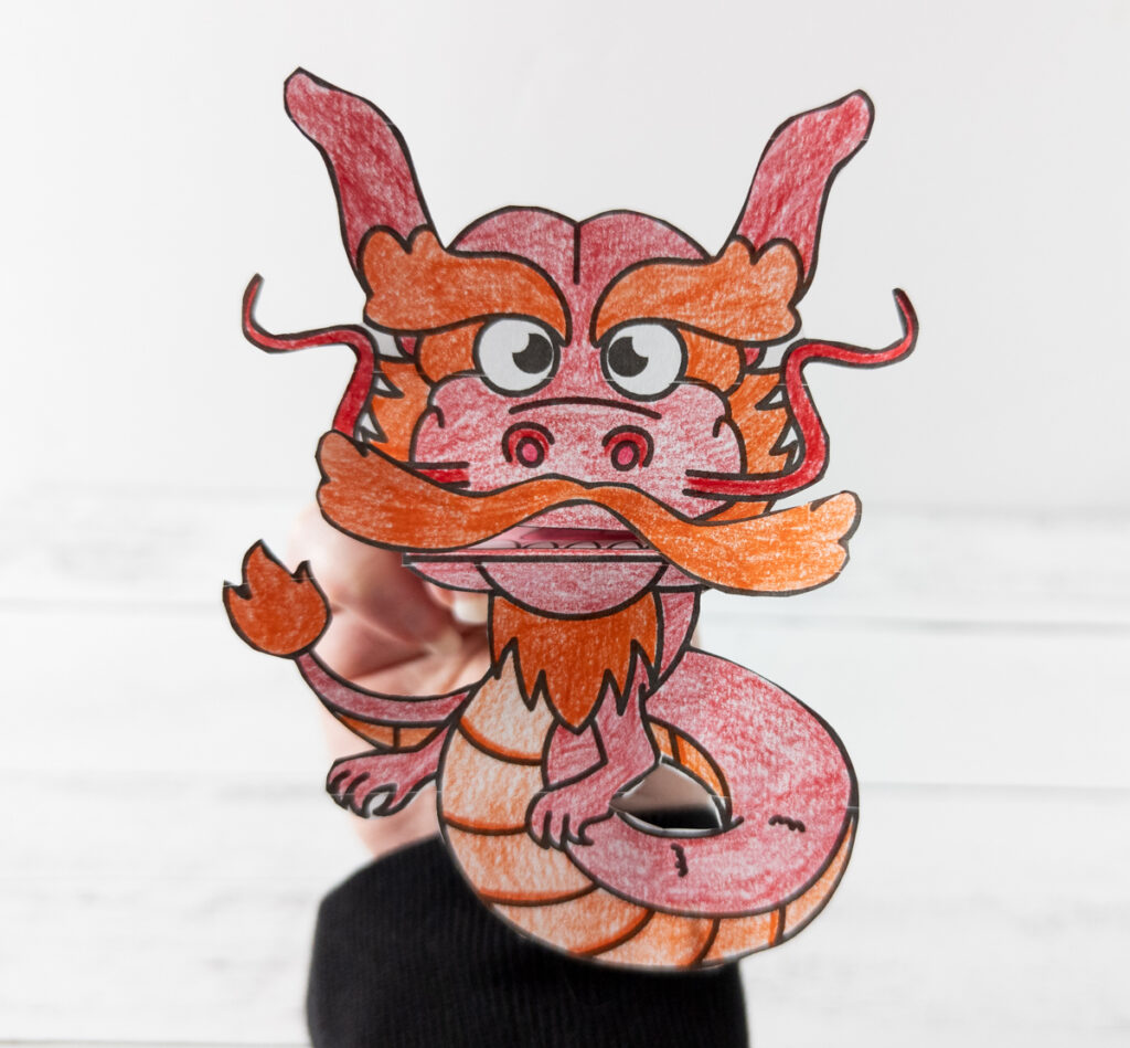 Hand holding up the red and orange printable dragon finger puppet craft.